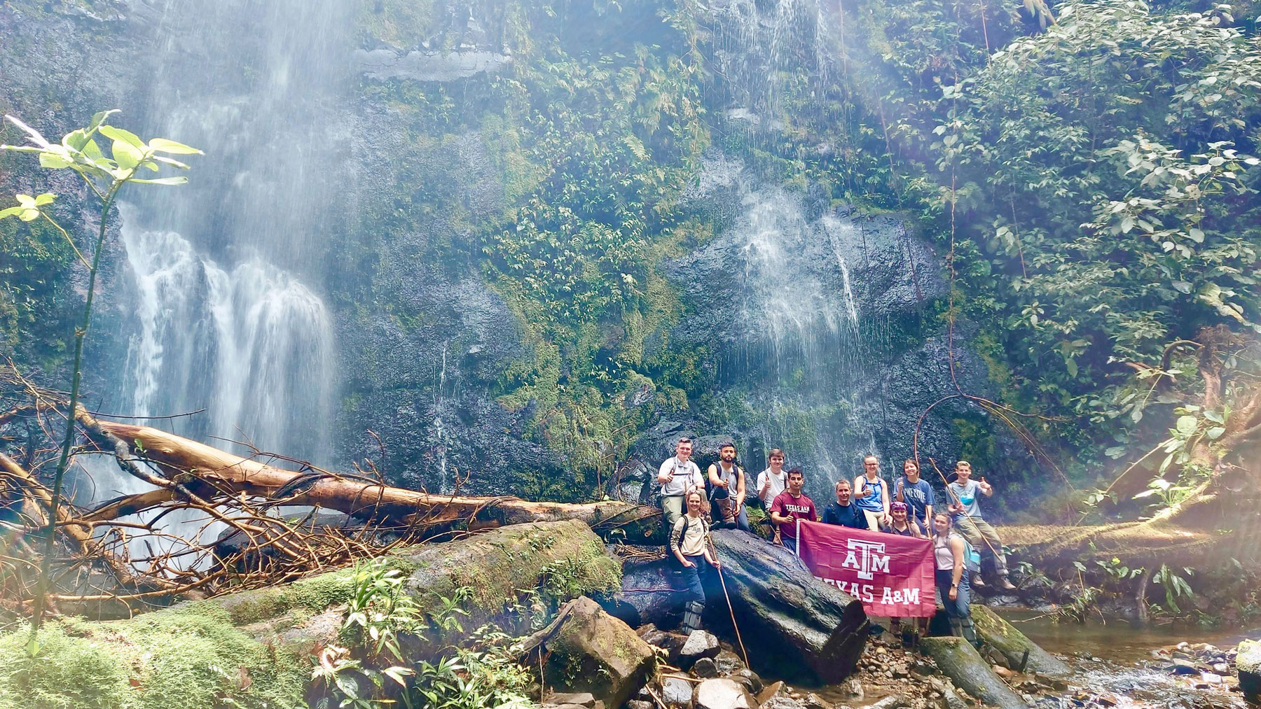 Group of students holding a Texas A&amp;M flag in front of a waterfall