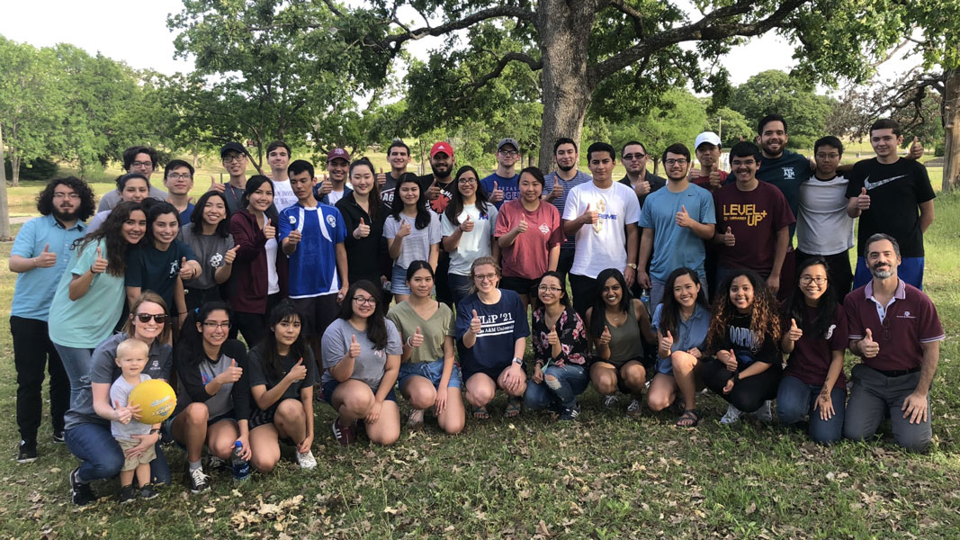 large group of college students standing outside under a tree