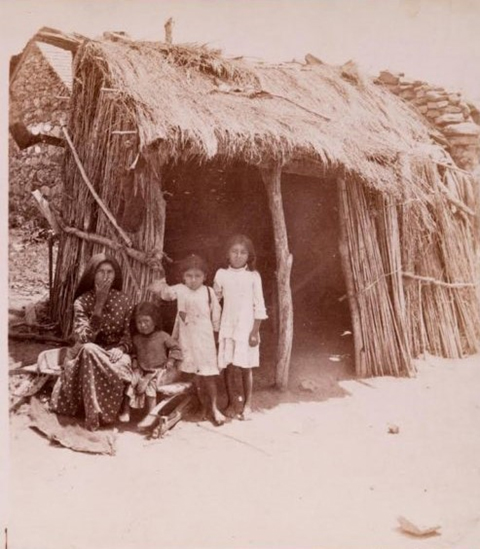 Native American family in front of their jacal (traditional Coahuiltecan-style house) in San Antonio, Texas, likely Mission San Francisco de la Espada, circa 1880.