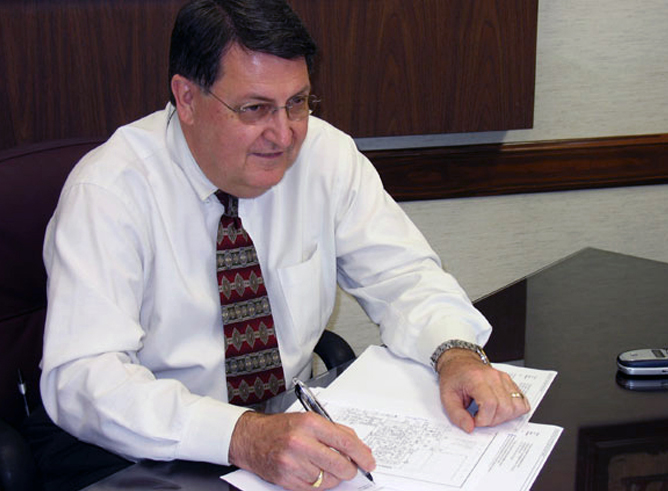 Texas A&M mathematician Richard Ewing smiles as he looks up from his paperwork with pen in hand.