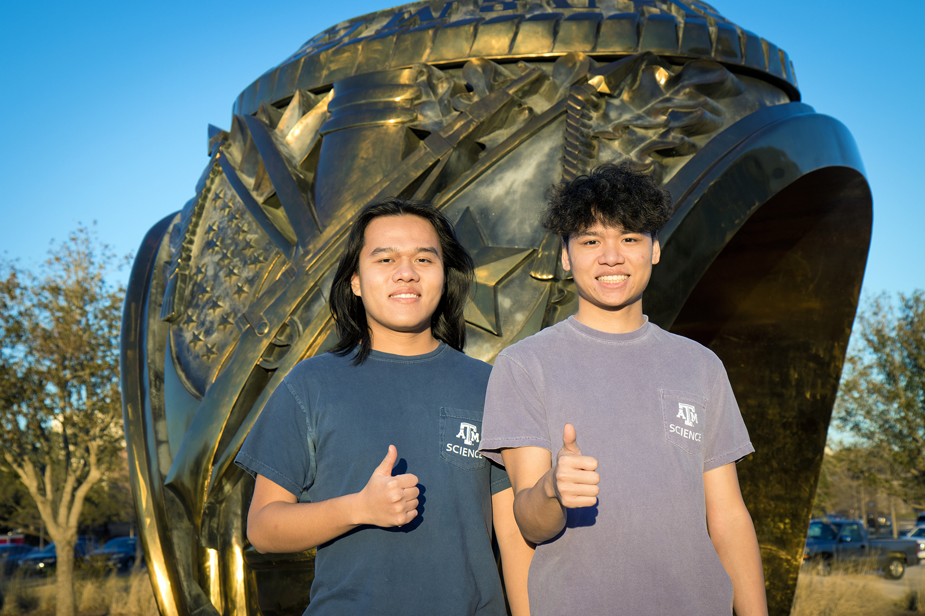 Texas A&M biology majors and brothers Henry and Kyle Nguyen flash a classic gig 'em in front of the Aggie Ring sculpture on the Texas A&M campus