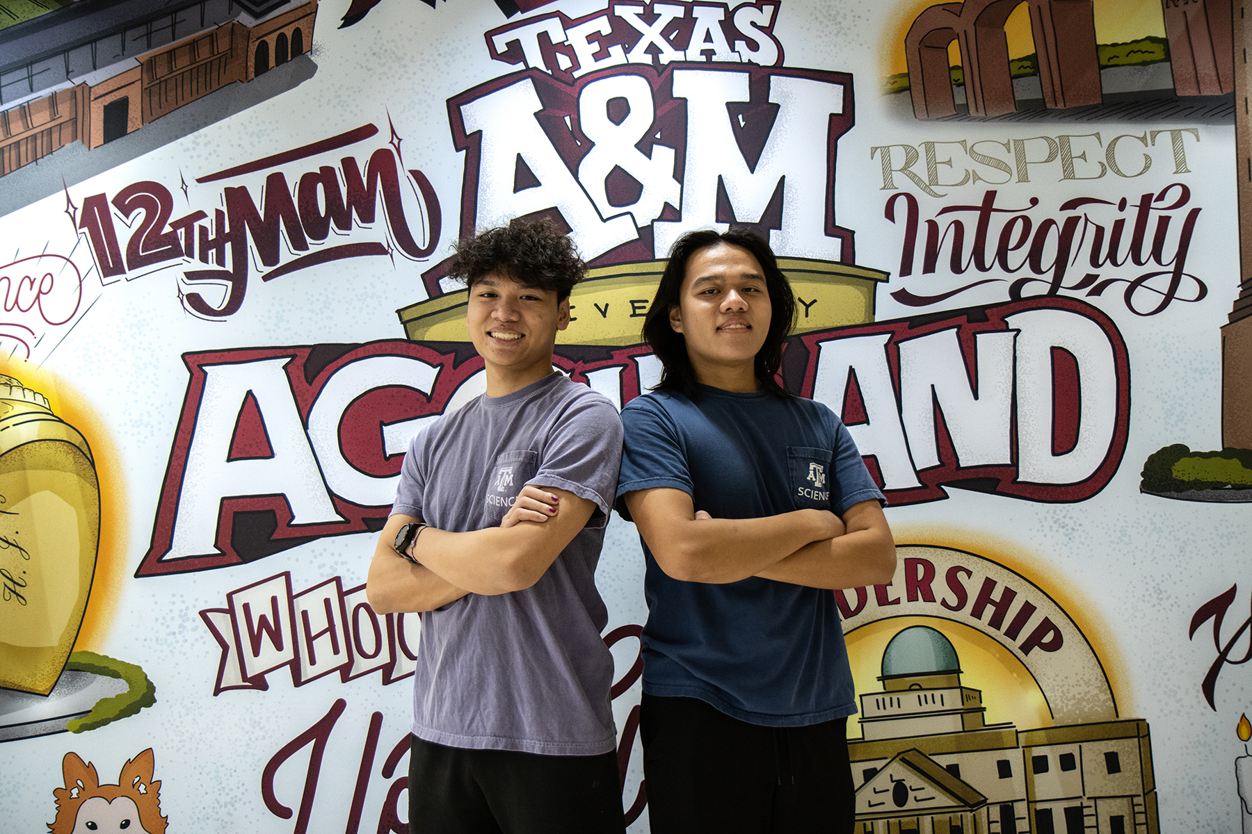 Texas A&M biology majors and brothers Kyle and Henry Nguyen pose with arms crossed in front of a Texas A&M-themed mural located in Rudder Tower on the Texas A&M University campus