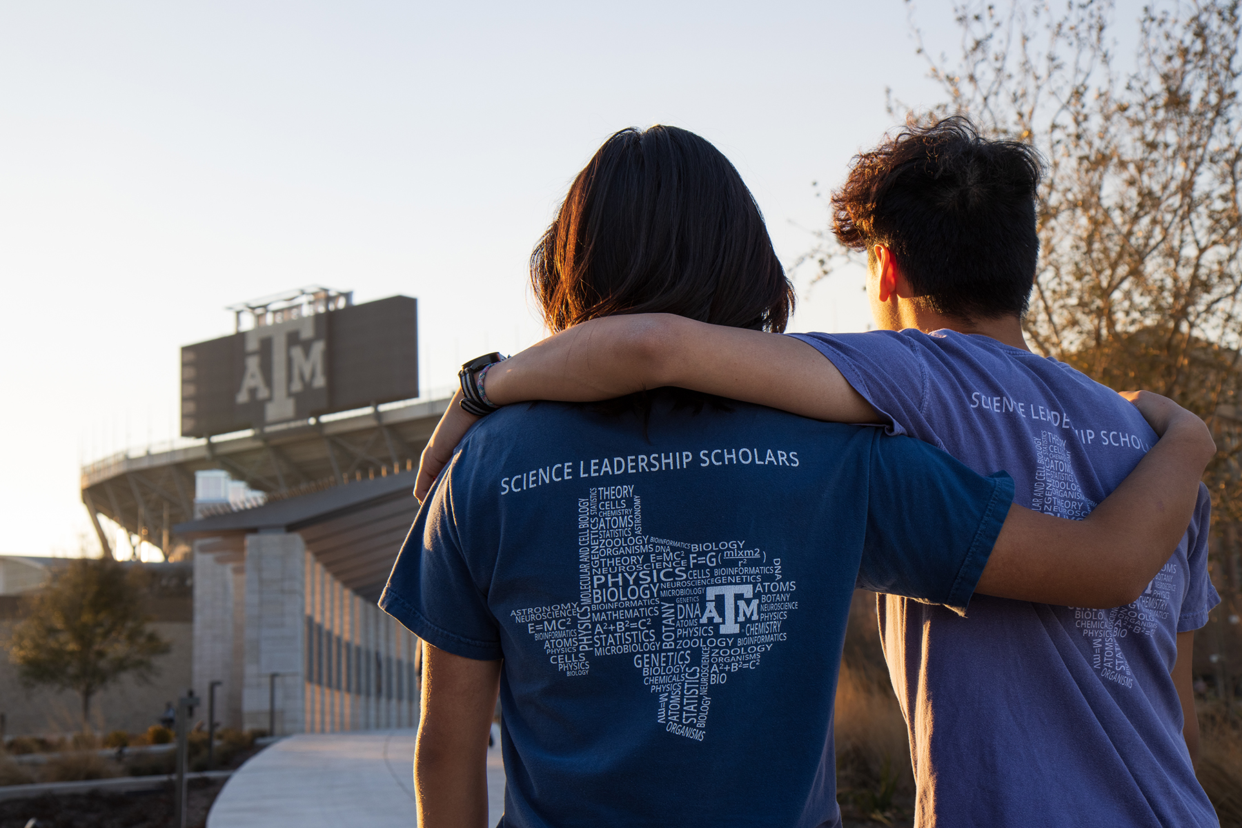 Texas A&M biology majors and brothers Henry and Kyle Nguyen stand arm in arm with their backs to the camera looking toward Kyle Field on the Texas A&M campus