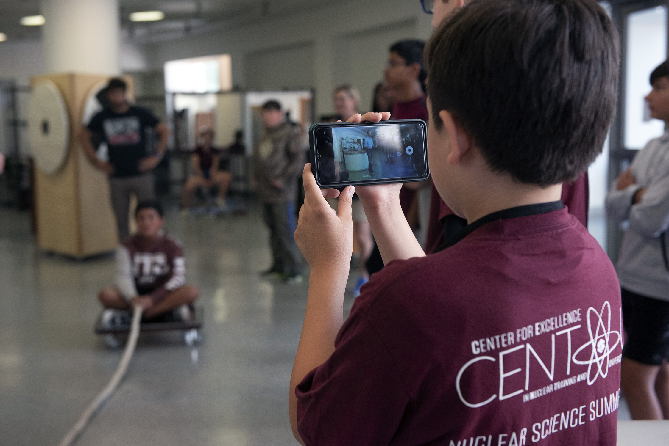 Middle school students wearing maroon CENTAUR t-shirts participate in hands-on science demonstrations during a nuclear science summer camp at Texas A&M University