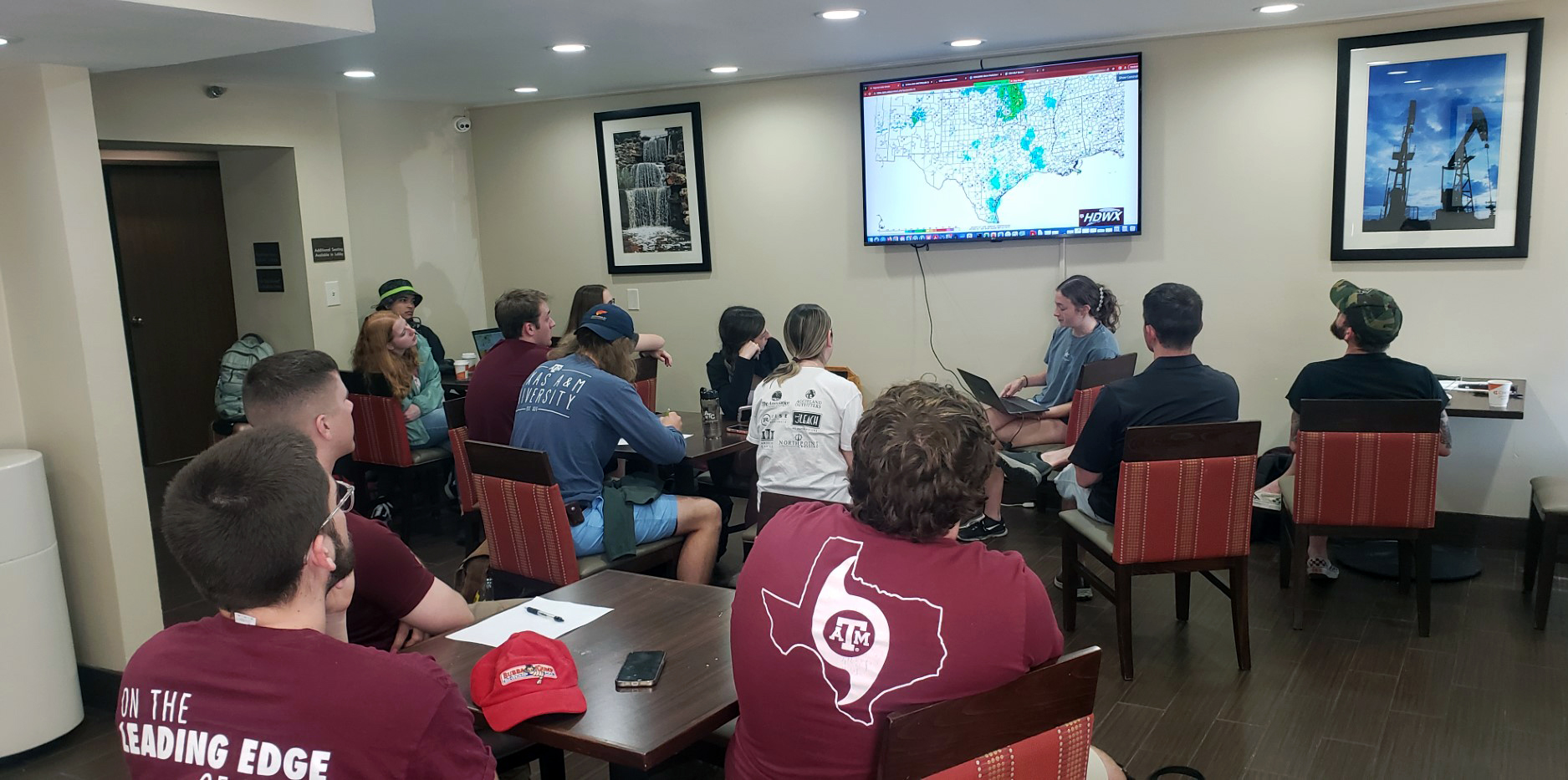 Texas A&M meteorology major Bailey Kropp sits with a laptop at the front of a group of seated students while leading a morning weather forecasting briefing in a hotel breakfast room in Wichita Falls, Texas