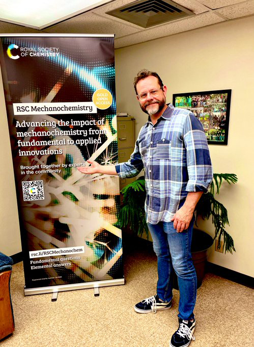 Texas A&M chemist James Batteas stands next to a pull-up banner promoting the new Royal Society of Chemistry journal RSC Mechanochemistry