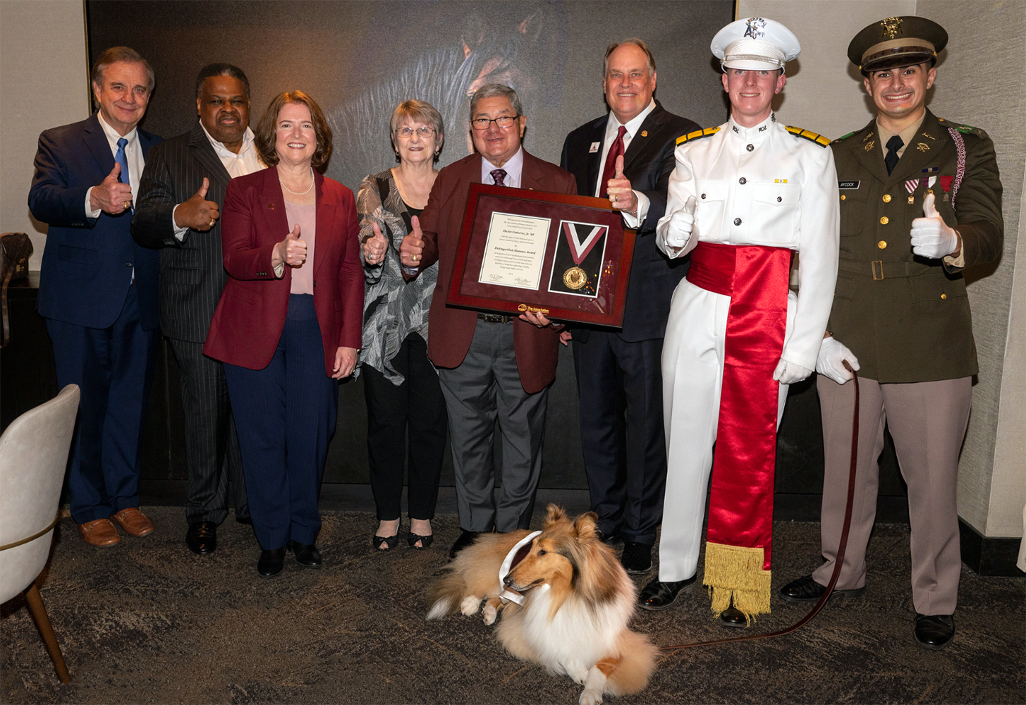 1969 Texas A&M mathematics graduate Hector Gutierrez Jr. and his wife Debbie Gutierrez flash gig 'ems while posing with various Texas A&M administrators during a surprise announcement of his 2023 Texas A&M University Distinguished Alumnus Award honor