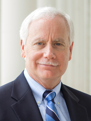 man with white hair and white mustache smiling at the camera in suit