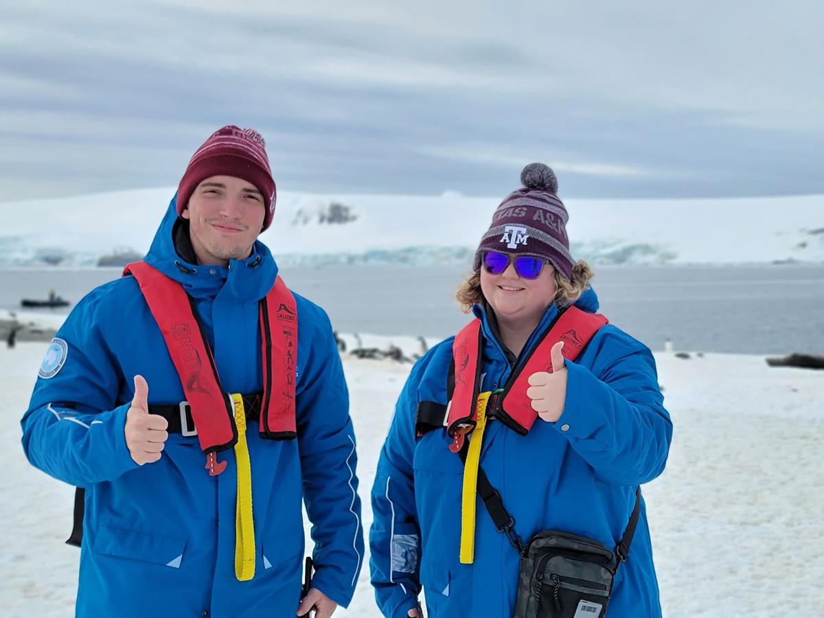 Two students participating in Texas A&M University's first study abroad trip to Antarctica in late fall 2023 flash smiles and thumbs-up gig 'em signs for the camera