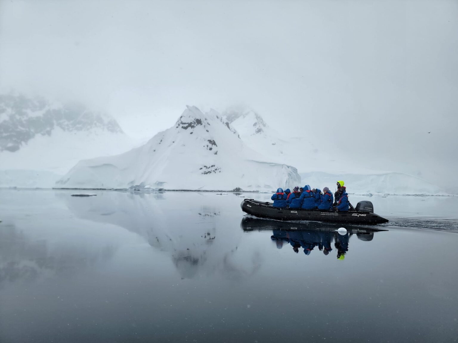 A small group of students, faculty and staff ride in a boat with snow-covered mountains in the background while on expedition during Texas A&M University's first study abroad trip to Antarctica in late fall 2023