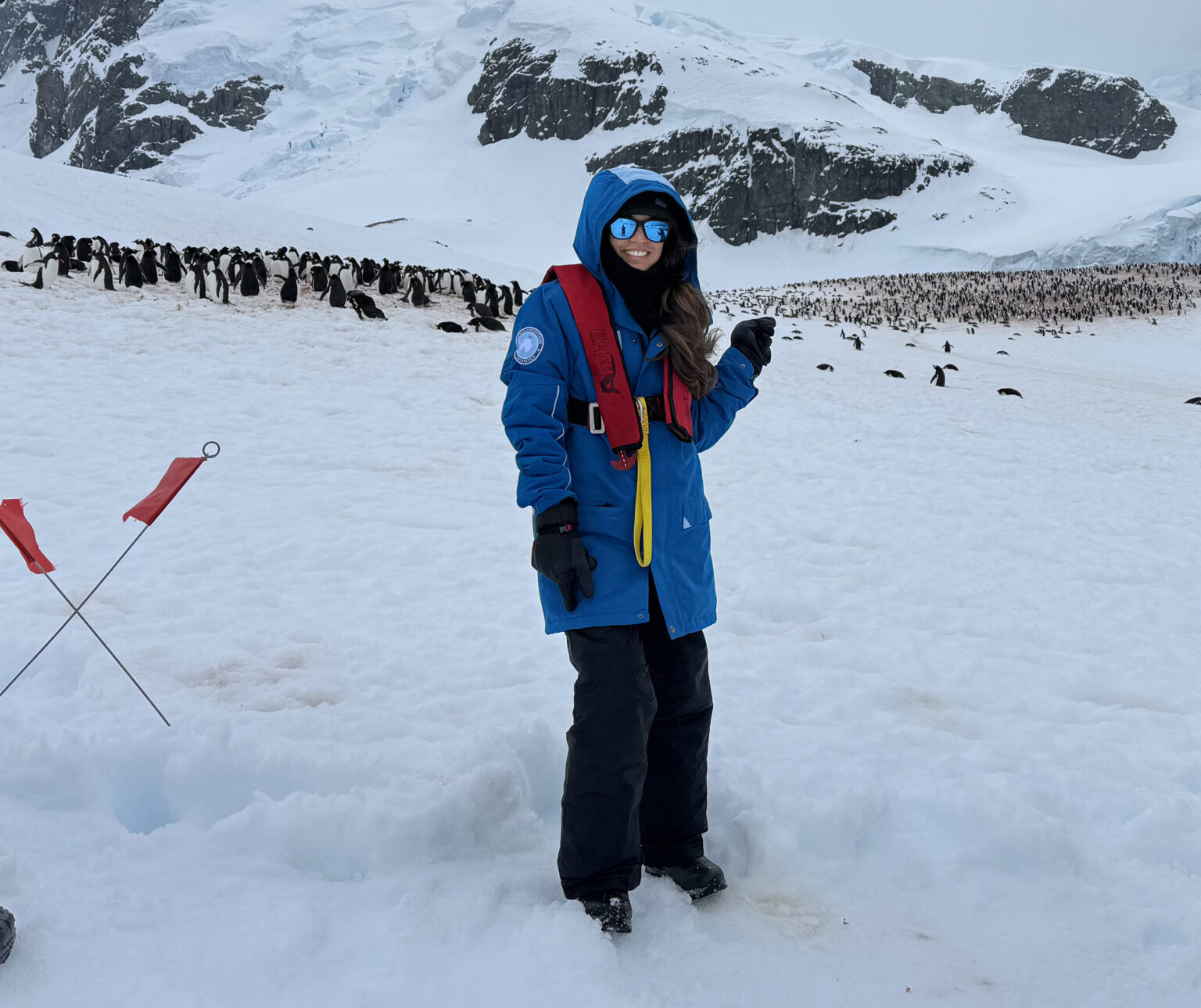 Veterinary graduate student Mary Chandra smiles against a backdrop of snow-covered mountains while pointing to a group of penguins gathered behind her during Texas A&M University's first study abroad trip to Antarctica in late fall 2023
