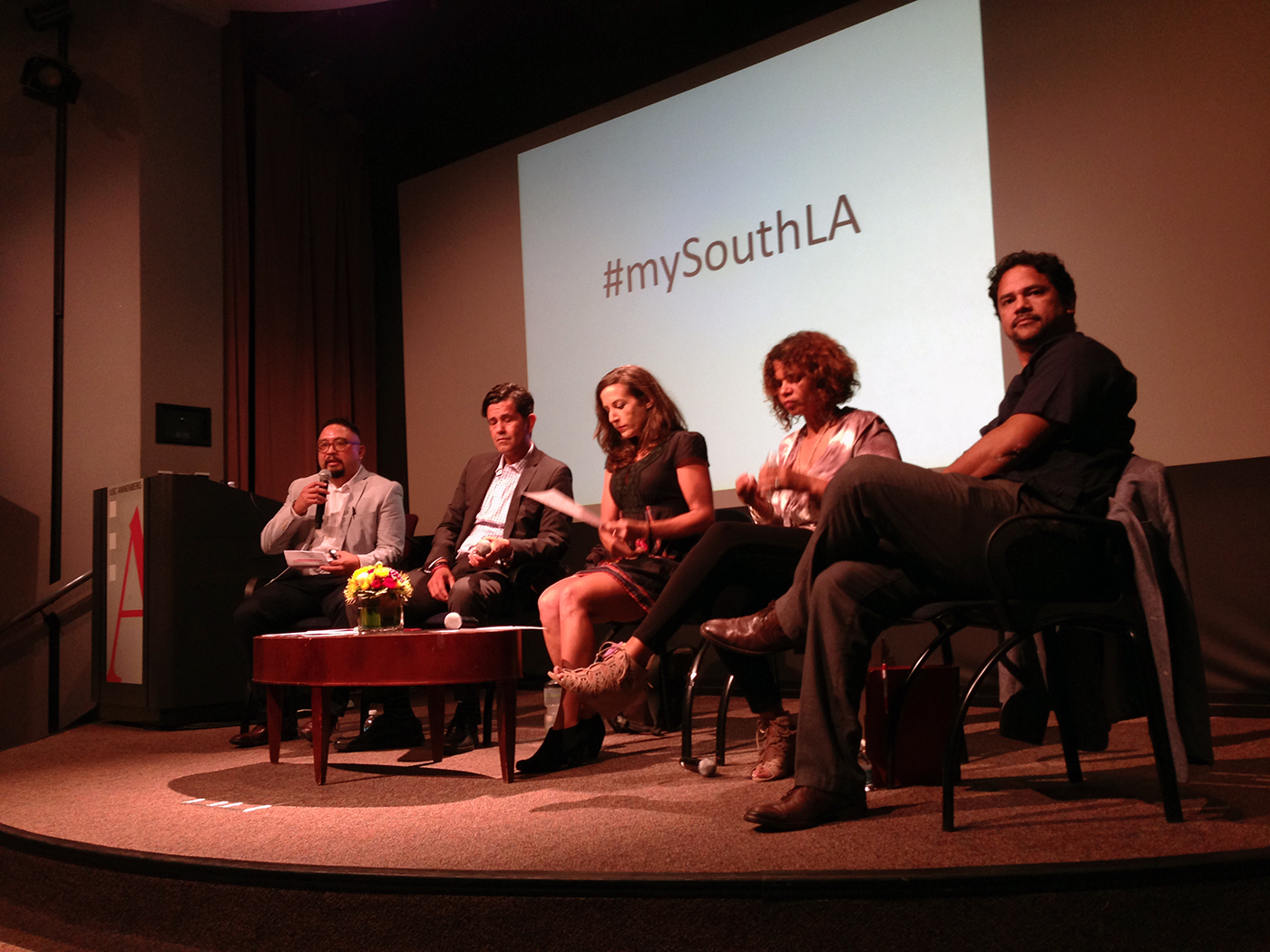 Texas A&M University communication professor George Villanueva sits on a stage along with four other speakers while moderating a panel of South Los Angeles community leaders and media producers during an event on the University of Southern California campus