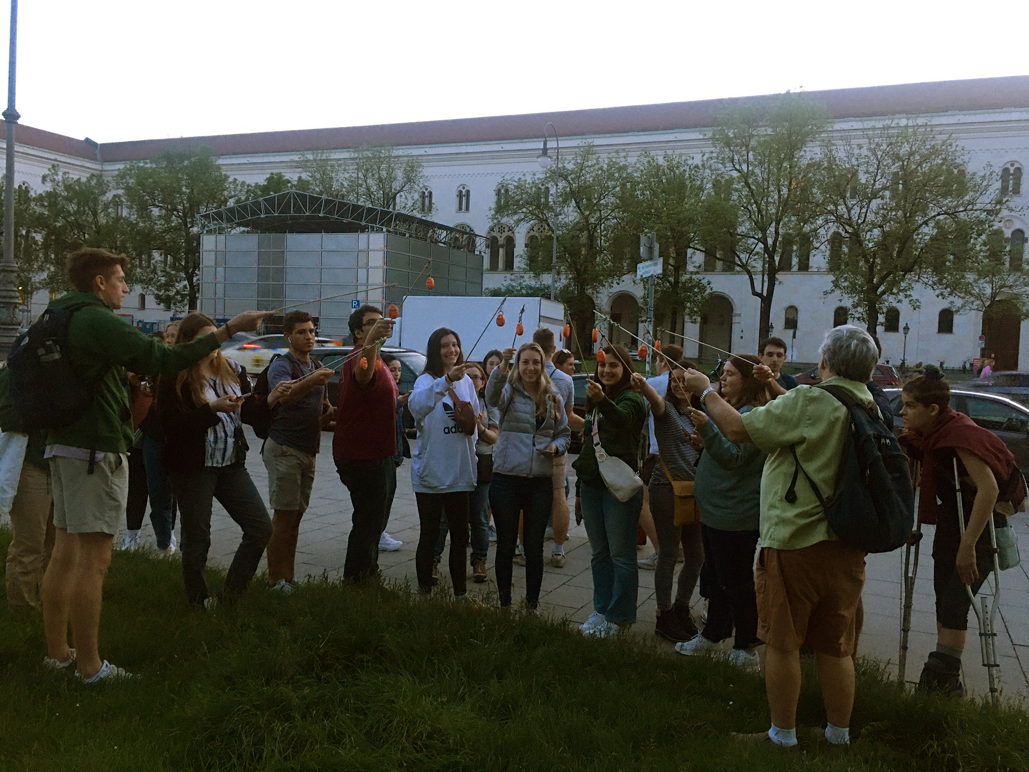 A group of Texas A&M University meteorology students in Munich, Germany, stand close together on a city street while using temperature and humidity loggers mounted on small poles to measure air temperatures and other atmospheric conditions for a research project on urban heat islands