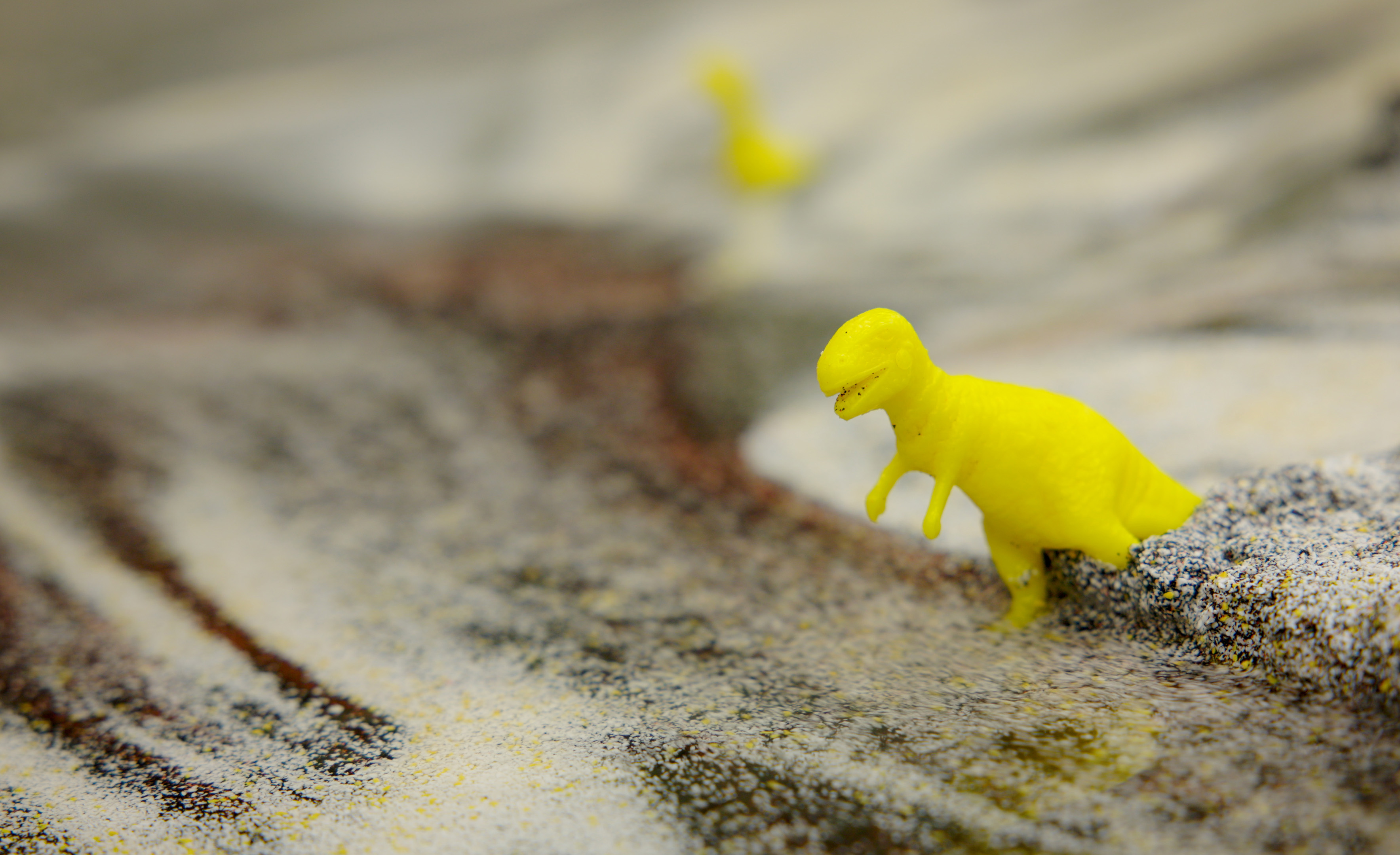 Close-up of a toy dinosaur in multicolored sand within the model landscape of a stream table in the Texas A&M University Department of Geology and Geophysics