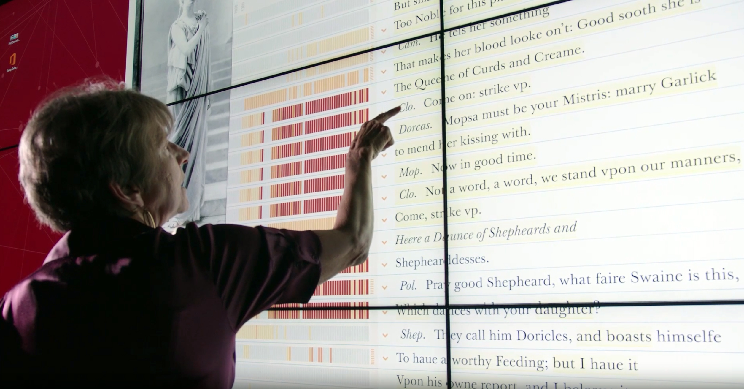 Texas A&M University English Professor Laura Mandell extends her index finger toward a wall-sized touch-screen display featuring the New Variorum Shakespeare website in the Humanities Visualization Space within the Center of Digital Humanities Research