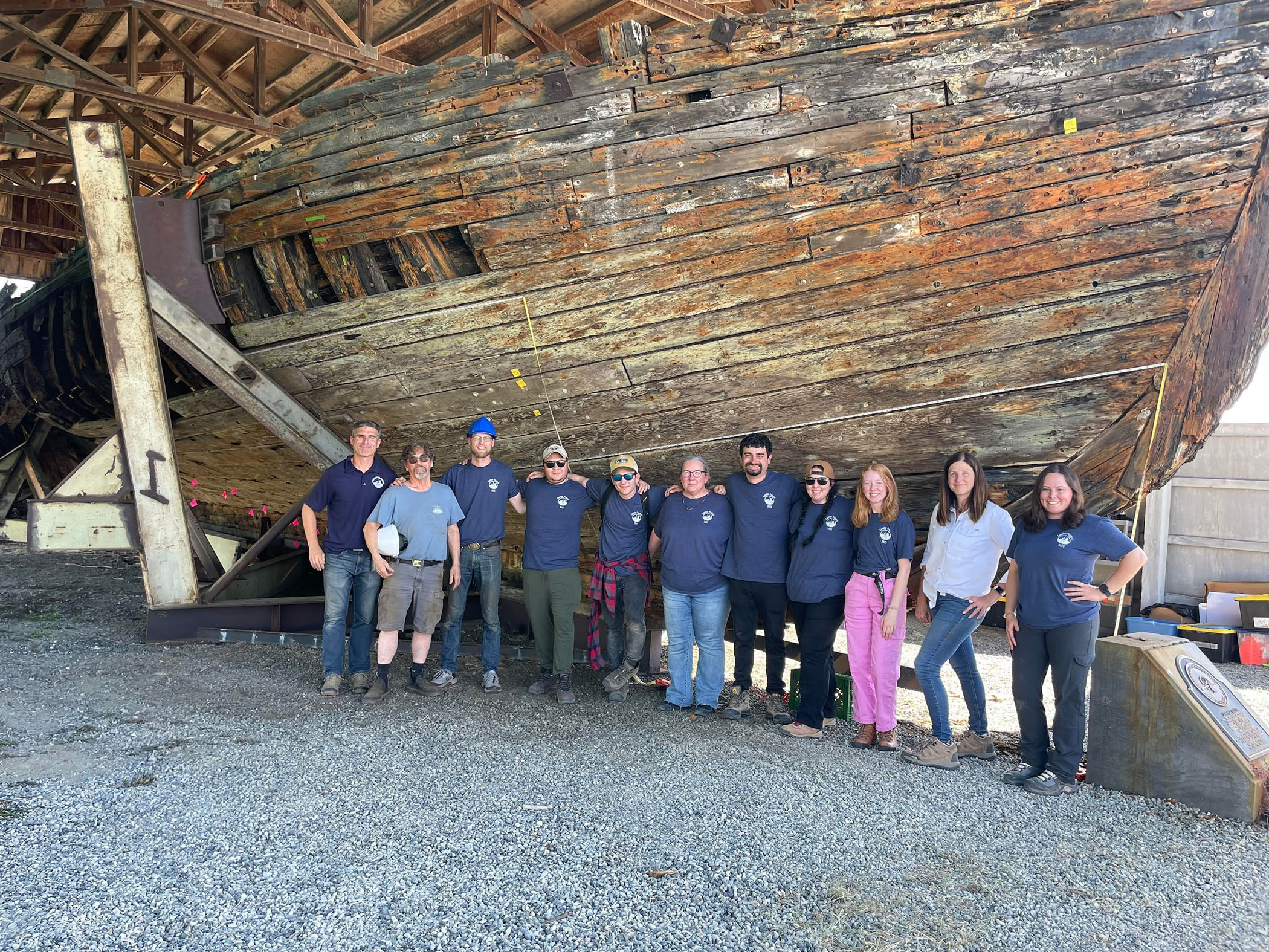 Group photo of the Texas A&M University nautical archaeology team standing in front of the Equator in dry dock in Everett, Washington, in 2023