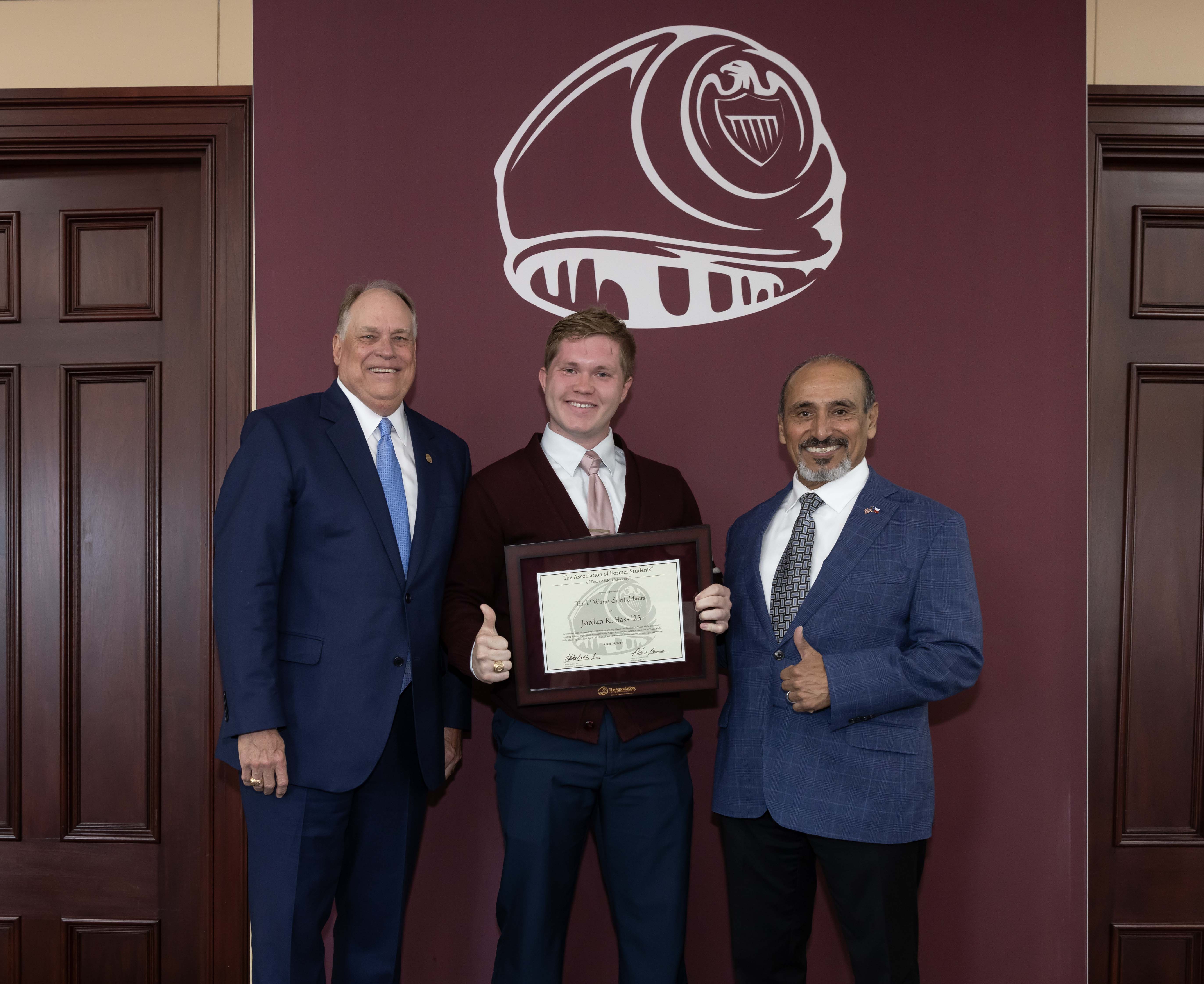 2024 Texas A&M University physics graduate Jordan Bass (center), posing with Porter S. Garner III '79, executive director of The Association of Former Students (left) and Brig. Gen. (Ret) Joe E. Ramirez Jr. '79, Texas A&M Vice President for Student Affairs, after receiving the 2024 Buck Weirus Spirit Award