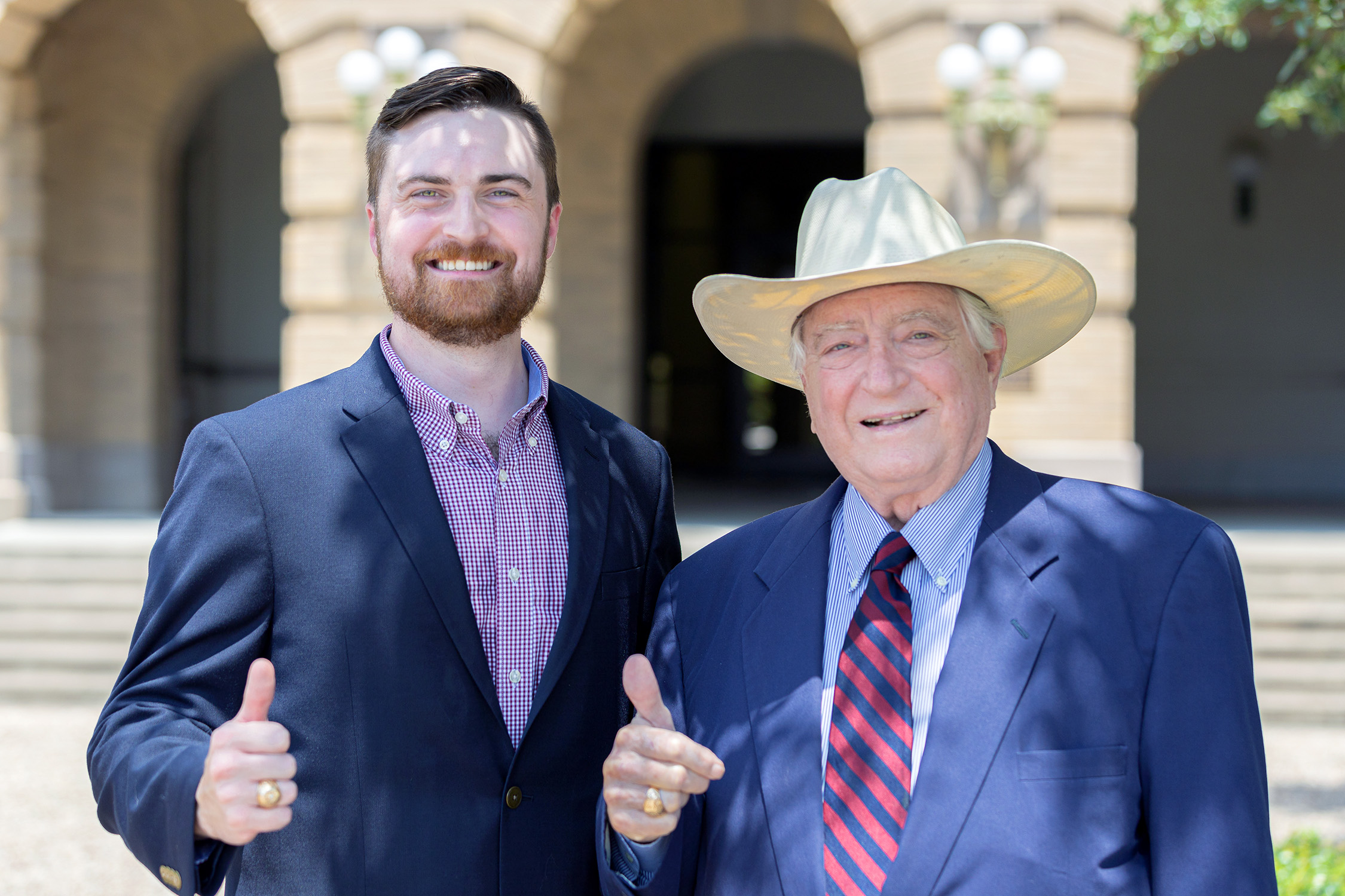 Luther Soules IV (left) and his father, Luke Soules flash an Aggie gig 'em/thumbs up for the camera outside the Academic Building on the Texas A&M University campus