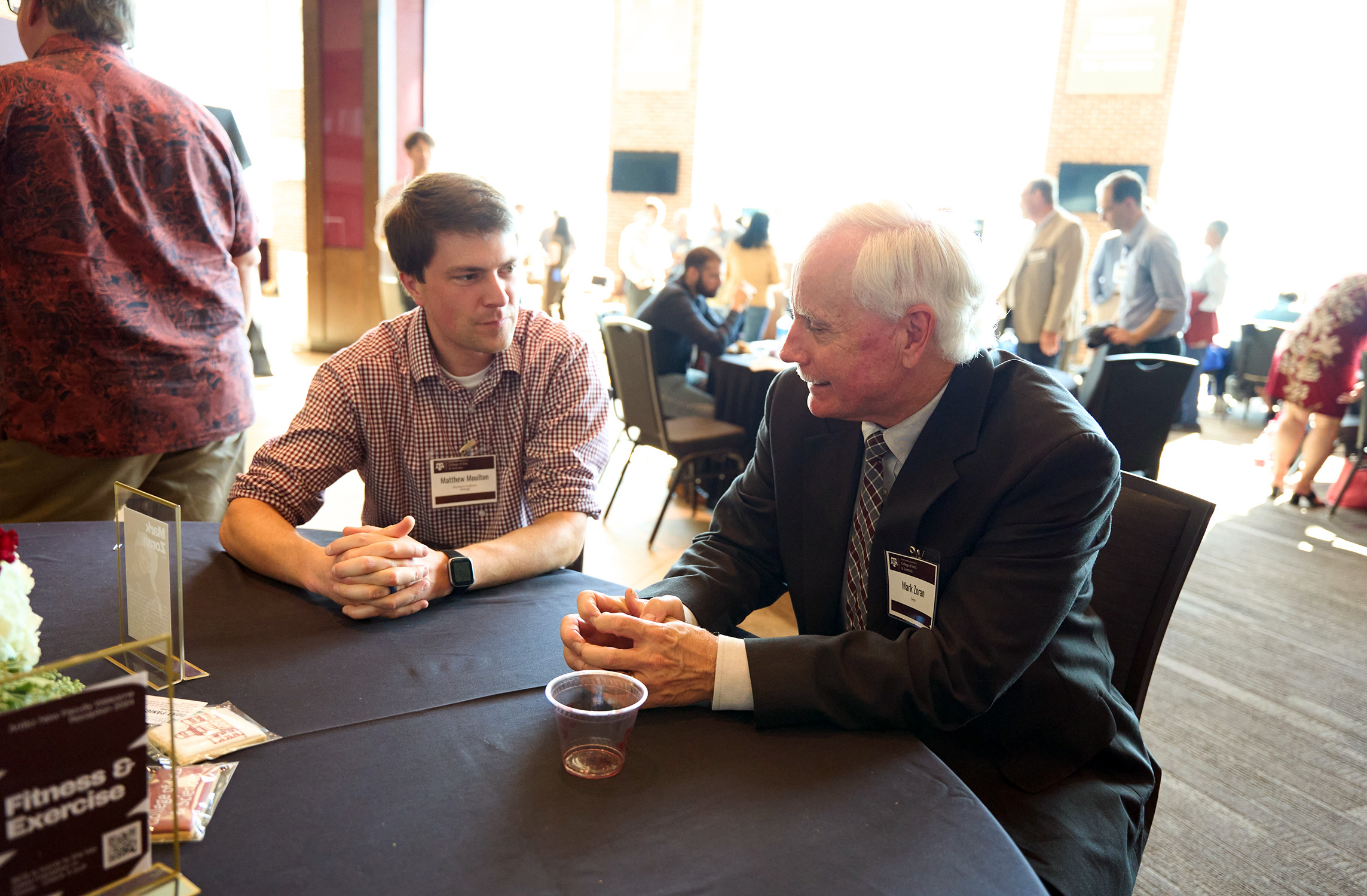 Texas A&M University biologist and College of Arts and Sciences Dean Mark Zoran (right) sits at a table, talking with fellow Texas A&M biologist Matthew Moulton
