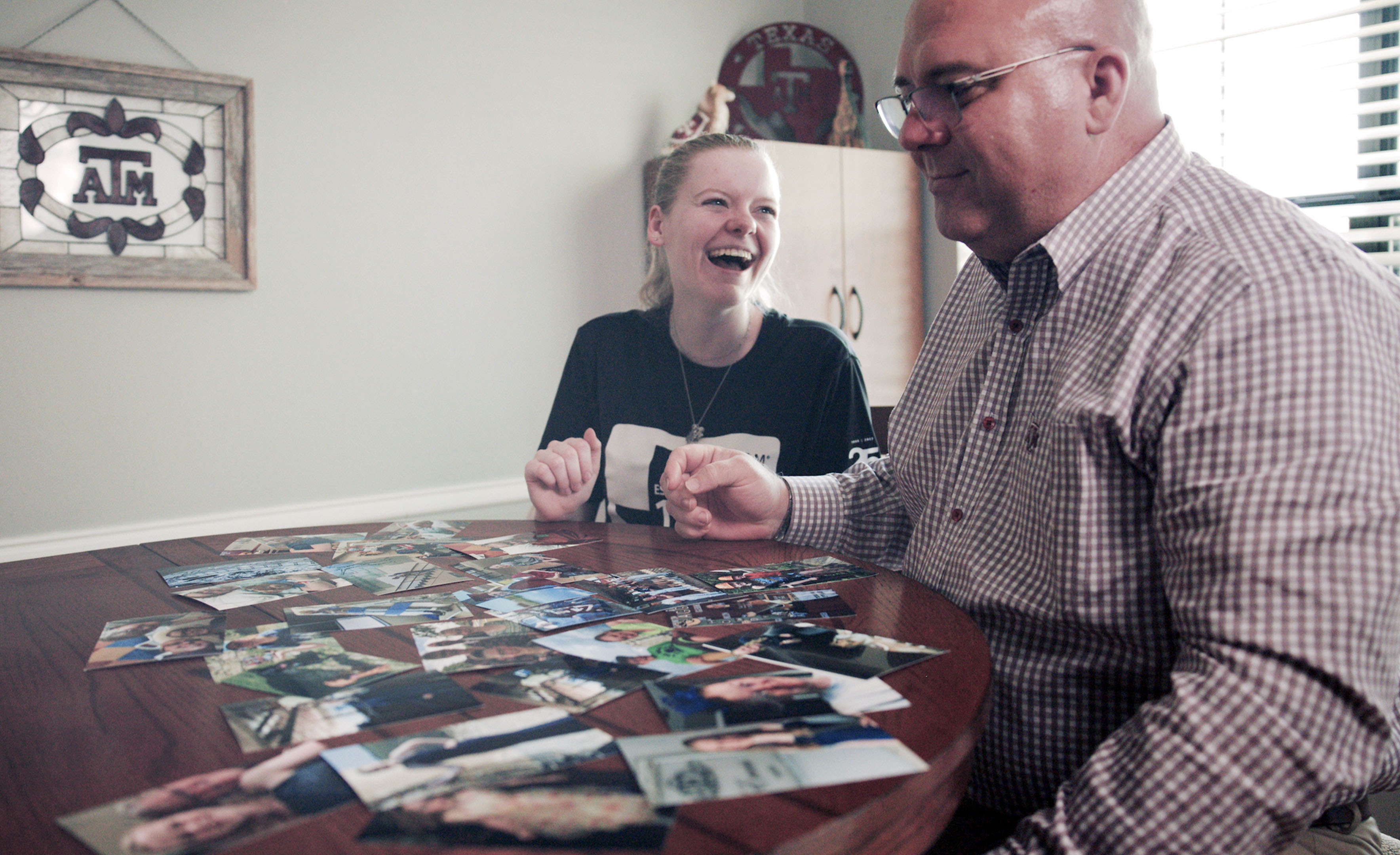 Texas A&M University allied health major Abbi Evans laughs while sitting with her dad, Ed Evans, at a kitchen table and looking through photographs spread out across the table