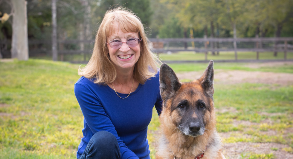 Person smiling in a park beside a German Shepherd.