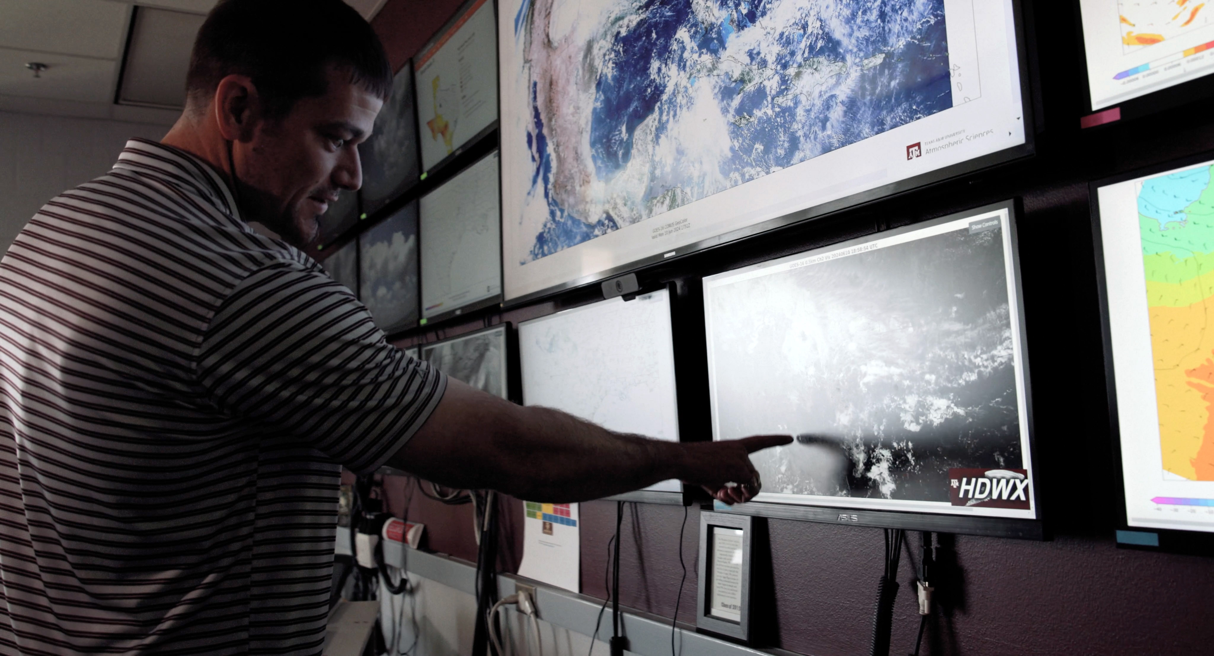 Texas A&M University atmospheric scientist Eric Nielsen points to a monitor on the wall within the Texas A&M Weather Center in the Department of Atmospheric Sciences