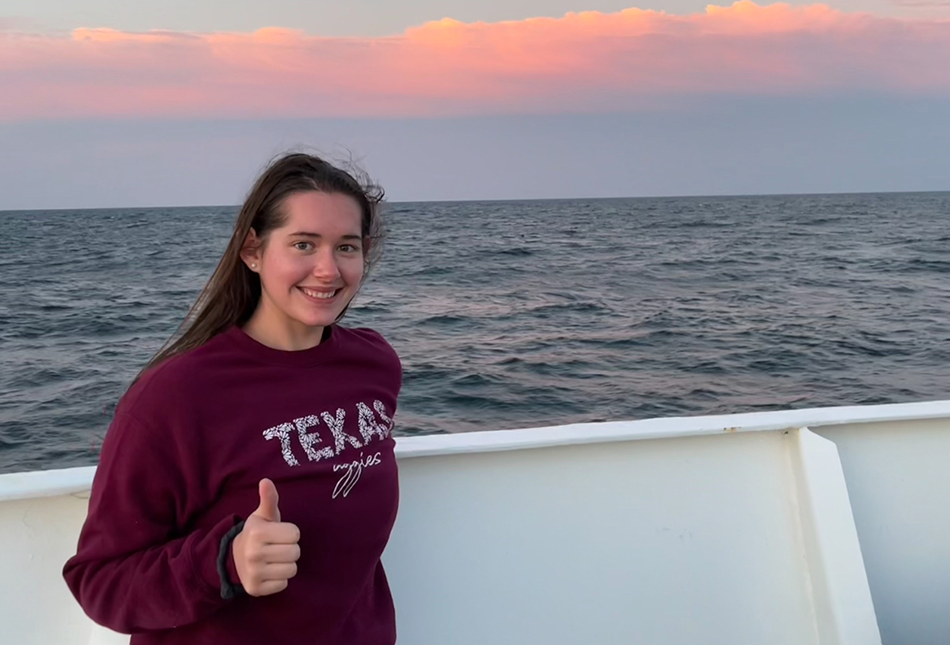 Kailey Rettmann giving a thumbs up aboard a recent Texas A&M Oceanography Schade Cruise at sunset with a "Texas A&M" sweatshirt on.