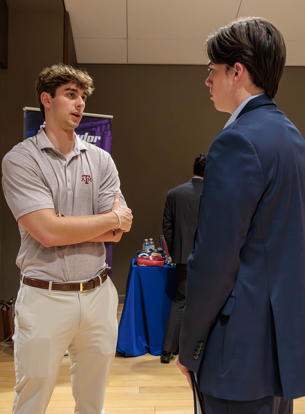 A representative from Matador dressed in a Texas A & M polo speaks with a student dressed in a suit.