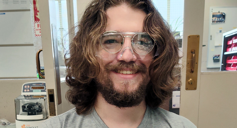 Texas A&M University physics graduate student Ryan Amberger, wearing goggles and smiling while in a laboratory at Argonne National Laboratory in 2024.