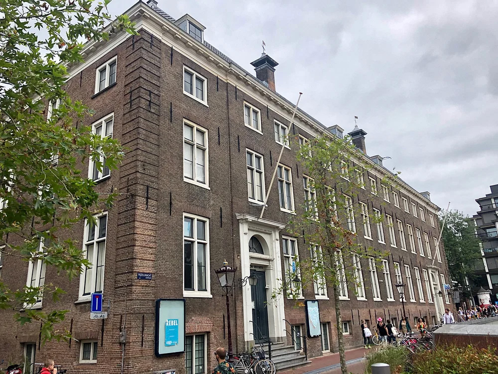 Exterior view of the Descartes home in Amsterdam, a historic brick building with multiple windows, surrounded by trees and bicycles parked along the street.