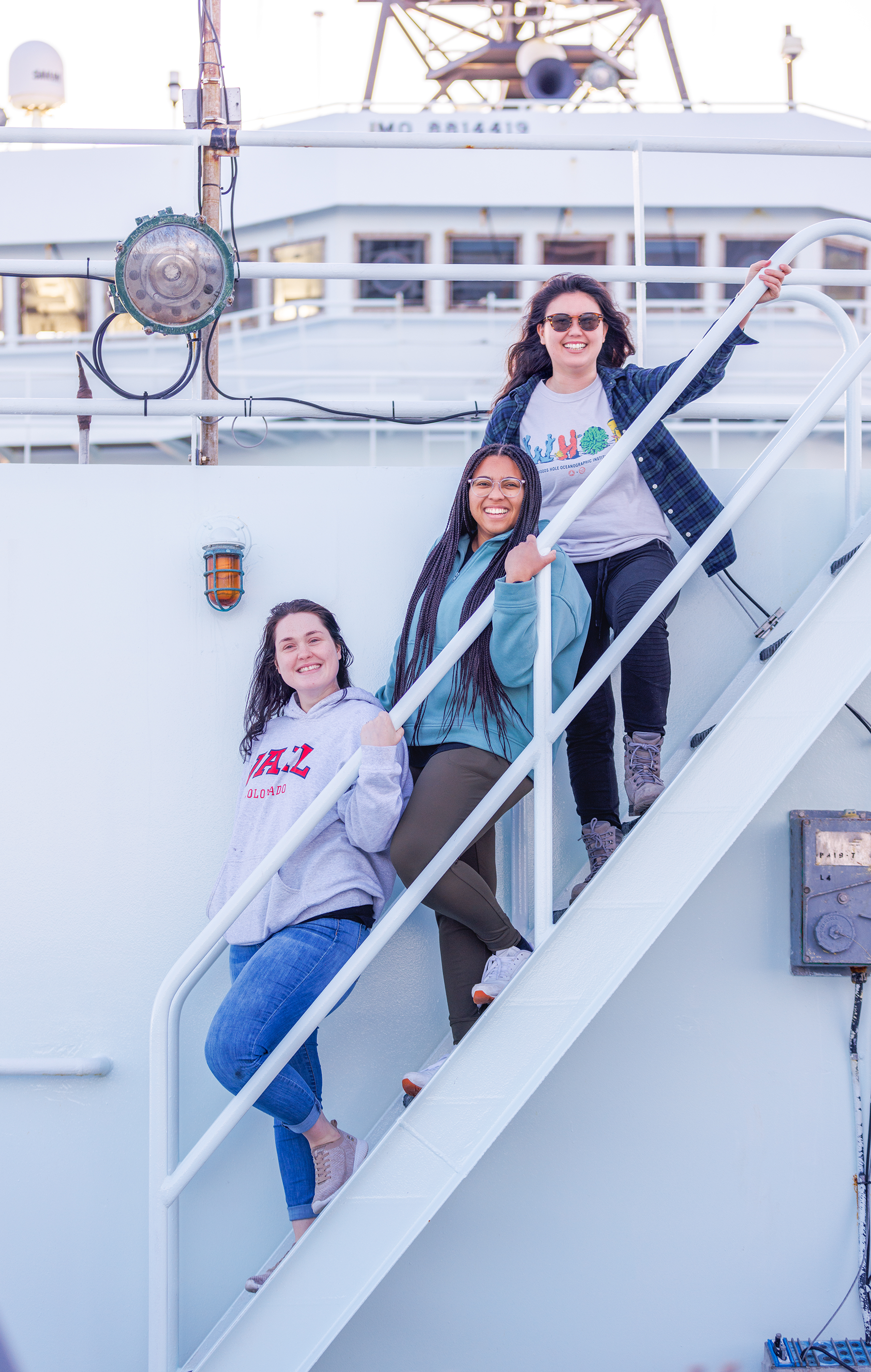 Three people smiling on a stairway aboard the ship "Sun Raider.