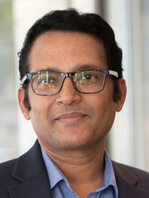 Portrait of a smiling professional wearing glasses and a navy blazer.