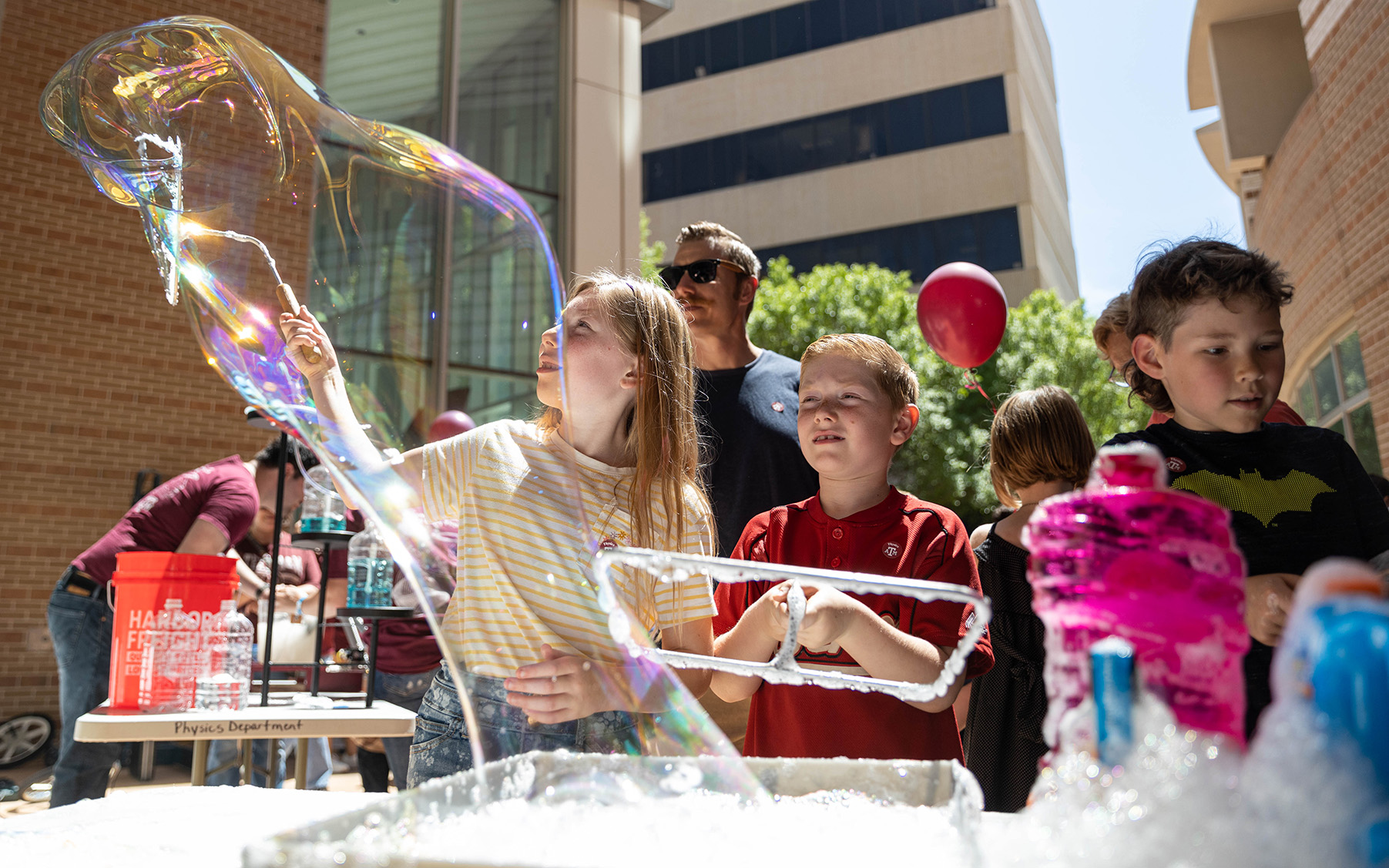 Young festival participants use metal tools to create large bubbles out of soap.