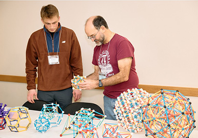 Two people examining geometric models on a table at a conference.
