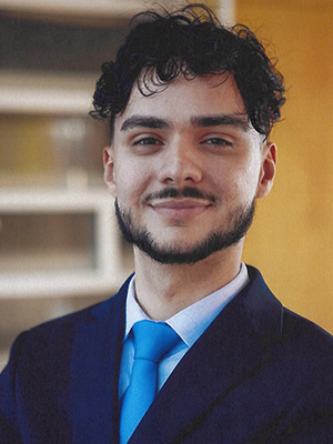 Deigo smiles, wearing a dark blue suit and blue tie.