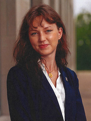 Ana Gou poses in front of the JKW Building, wearing a dark suit and white shirt.
