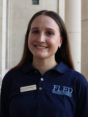 Jayden poses in front of marble columns, wearing a blue collered shirt with the FLED logo.