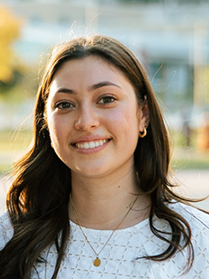 Katie smiles, wearing a white shirt and gold necklace.