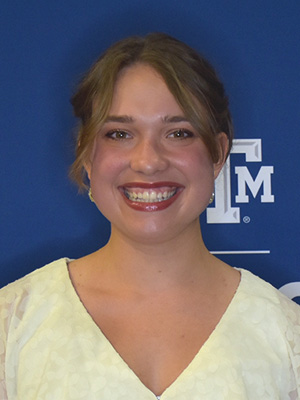 Madeline smiles in front of blue backdrop, partially showing the Texas A&M logo.